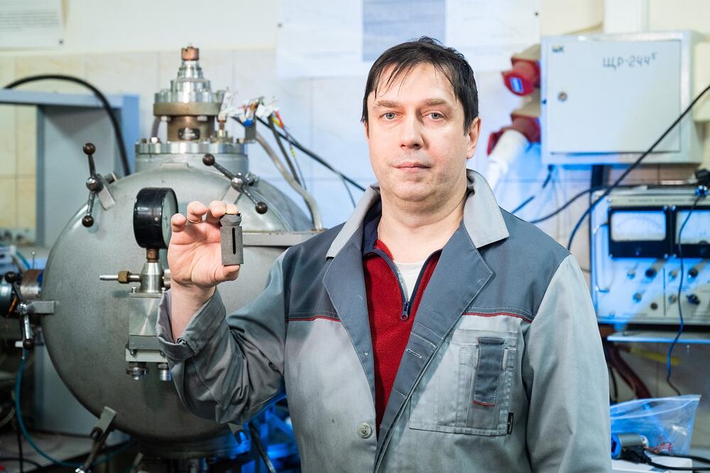 Сергей Жевненко держит в руках вольфрамовый нагреватель на фоне лабораторного оборудования